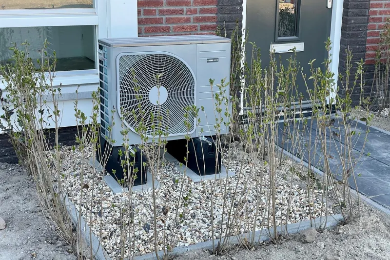 Unidad exterior de una bomba de calor de aerotermia instalada junto a la fachada de una casa